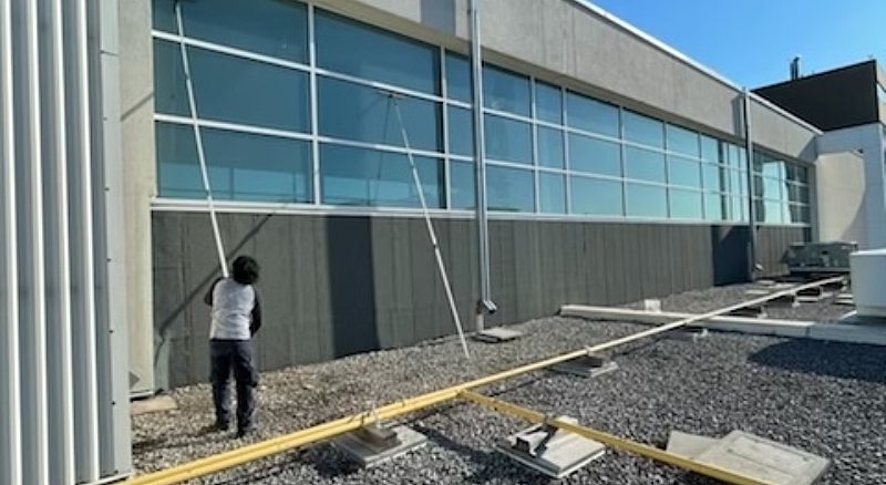 Worker using a Tucker pole for cleaning glass on an industrial rooftop, ensuring spotless windows from a distance