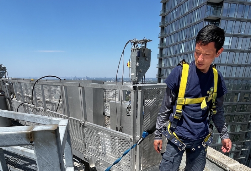 Employee safely secured to a swing stage, ready to begin high-rise window cleaning on a commercial building