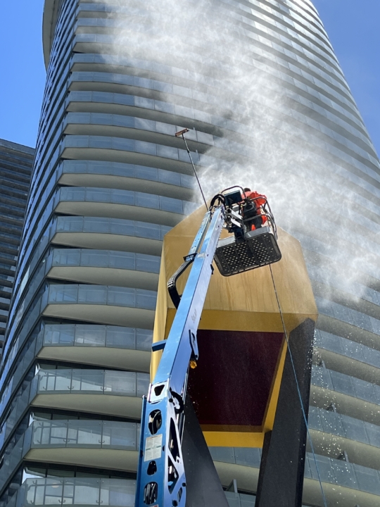 Pressure washing in progress with an elevated platform lift, cleaning the exterior of a tall building