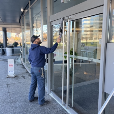 Window cleaning at the entrance of a commercial building, with a worker using a squeegee to clean the glass windows