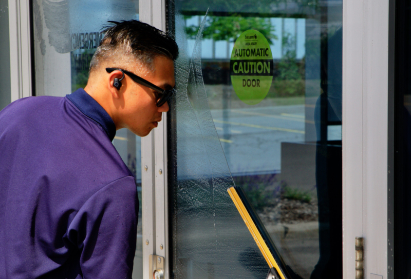 Professional window cleaning at ground level of an industrial  building, with a worker using a squeegee