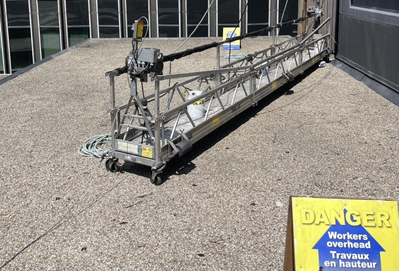 Altrex swing stage on the ground next to a Solar Group Inc sign, ready for high-rise window cleaning